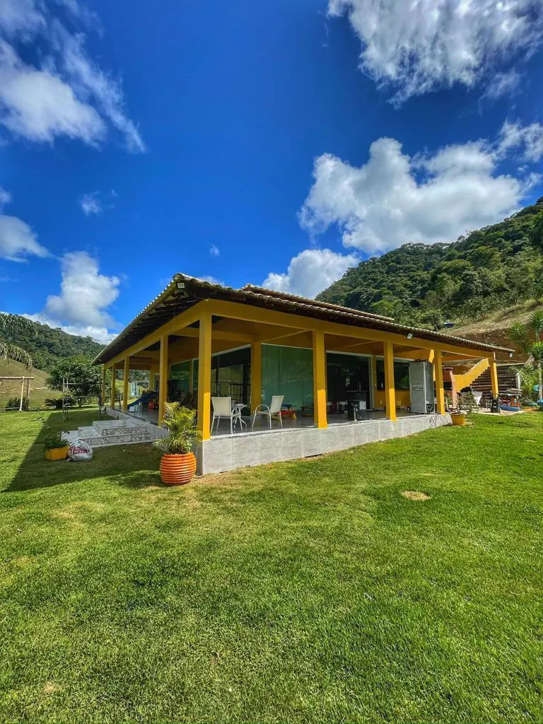 Vista diurna do Rancho Gentileza com casa amarela e palmeiras